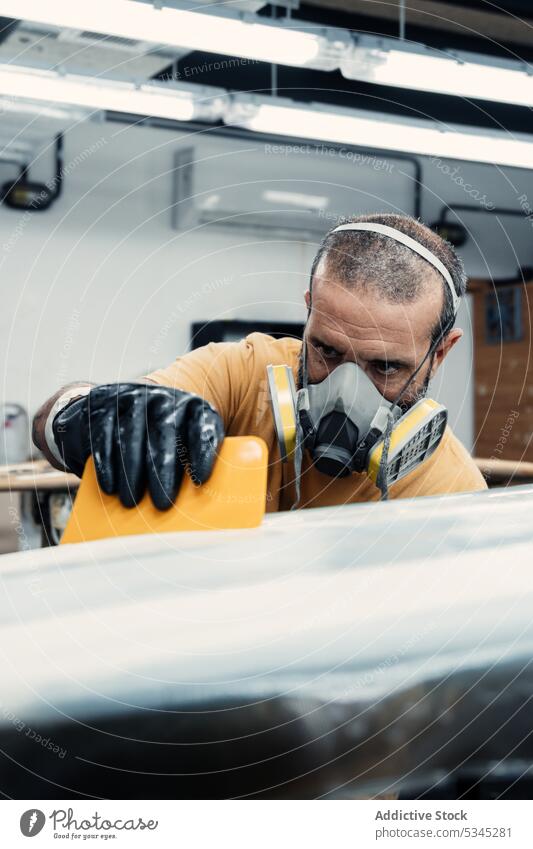 Seriöser Mann, der einen Film auf einem Surfbrett befestigt Form Atemschutzgerät behüten Werkstatt Arbeit Meister befestigen Fiberglas sanft Schaber Mundschutz