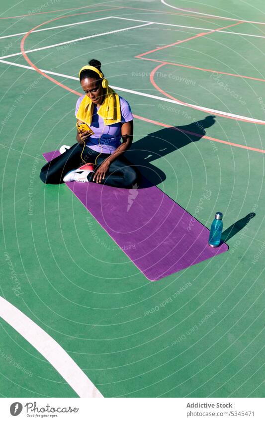 Eine fitte schwarze Sportlerin benutzt nach dem Training ihr Smartphone auf der Matte Frau Athlet Musik benutzend Sportpark Pause zuhören Erwachsener