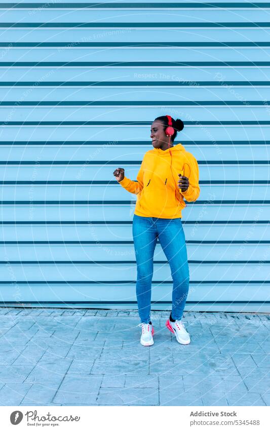 Stilvolle junge Dame mit Kopfhörern tanzt auf der Straße zuhören Großstadt lässig Musik Smartphone Frau Wand Gerät Afroamerikaner Gesang urban ethnisch modern