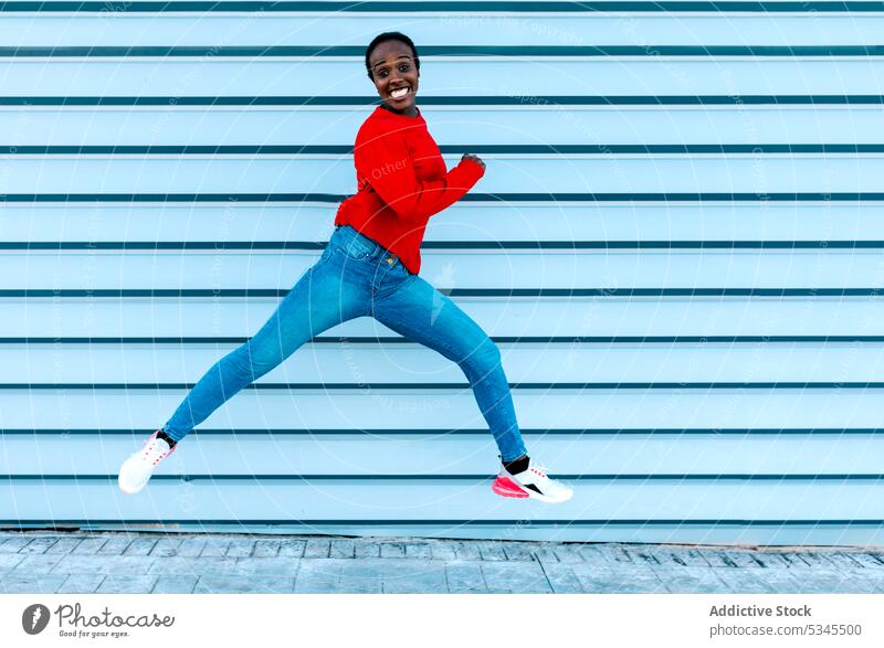 Fröhliche Frau springt auf dem Bürgersteig Model springen Sprung Lächeln aufgeregt Freude Großstadt Straße schwarz Afroamerikaner Energie dynamisch