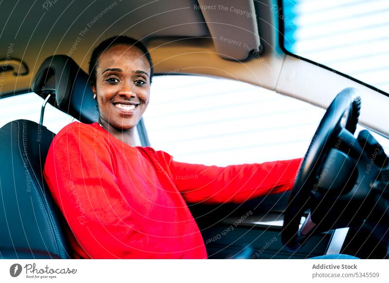 Lächelnde ethnische Dame schaut in die Kamera im Auto Frau PKW Fahrer Fahrzeug Inhalt heiter Automobil selbstbewusst positiv froh Afroamerikaner schwarz