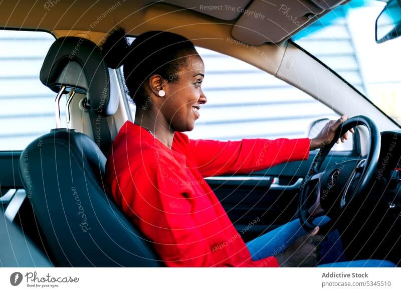 Lächelnde ethnische Dame am Steuer eines Autos Frau PKW Fahrer Fahrzeug Inhalt heiter Automobil selbstbewusst positiv froh Afroamerikaner schwarz Erwachsener
