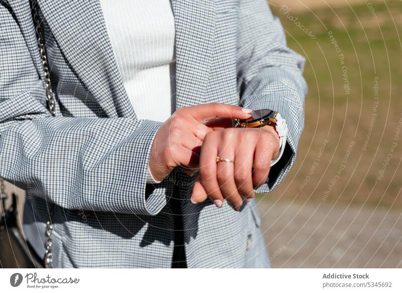 Unbekannte Frau berührt Armbanduhr, während sie im Park steht Zeit prüfen punktuell Großstadt Spaziergang kariert Sommer Stil Natur Straße Jacke trendy spät