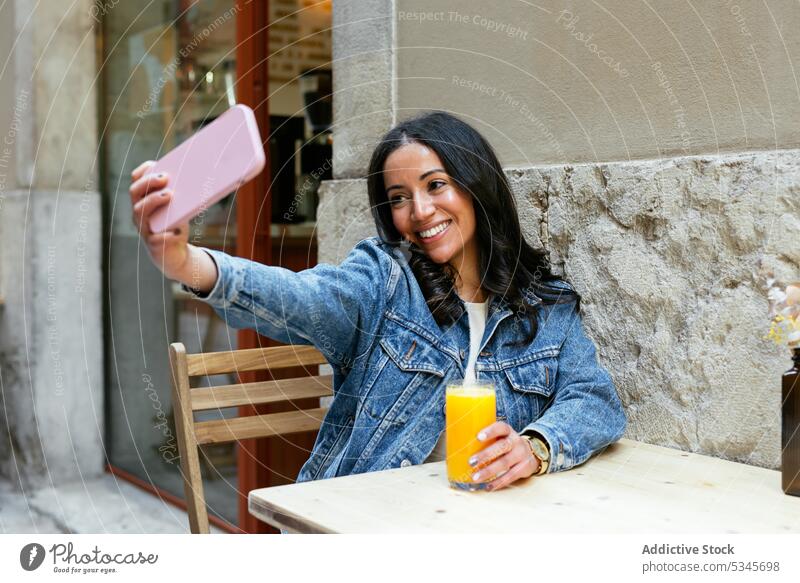 Fröhliche ethnische Frau macht Selfie am Tisch Smartphone Café Saft Straße Lächeln benutzend positiv Moment Glück jung Mobile hispanisch Apparatur Gerät