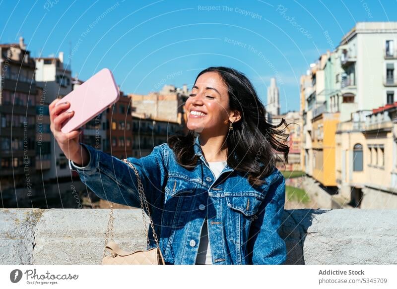 Lächelnde ethnische Frau steht auf dem Dach und macht ein Selfie Smartphone benutzend urban Gebäude Dachterrasse Begrenzung Wand jung Glück Mobile Telefon