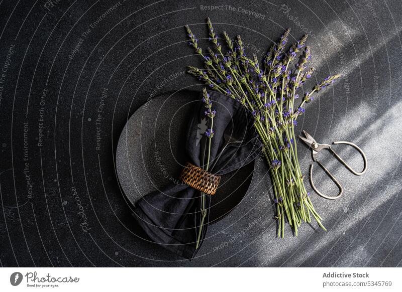 Hohe Winkel der Sommer-Tabelle mit Lavendel Blumen auf schwarzem Beton dunklen Hintergrund zwischen einer Serviette auf dem Teller und Schere Blumenstrauß