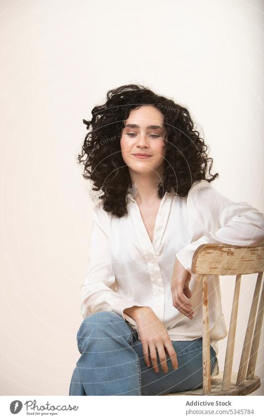 Junge Frau sitzt auf einem Holzstuhl im Atelier Beine gekreuzt Stuhl krause Haare Porträt Stil selbstbewusst lässig Vorschein jung Jeanshose Model Windstille