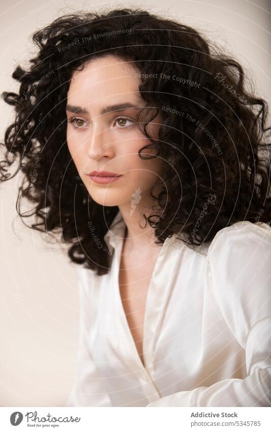 Nachdenkliche Frau mit lockigem Haar vor weißem Hintergrund Porträt besinnlich ernst Windstille nachdenklich Vorschein krause Haare Studioaufnahme jung Model