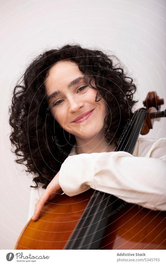 Glückliche Frau mit Cello im Musikstudio Musiker Instrument Porträt Lächeln Atelier Windstille froh Fähigkeit Melodie krause Haare Freude Hobby sitzen