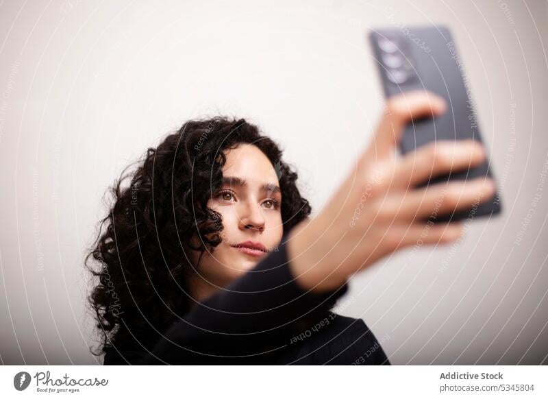 Emotionslose Frau macht Selfie im Haus Smartphone Sofa Porträt Mobile Telefon Gerät Selbstportrait Raum benutzend Apparatur krause Haare ernst formal Liege