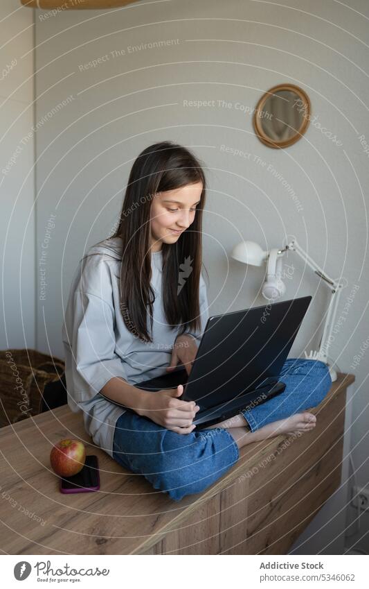 Lächelndes Teenager-Mädchen mit Laptop auf dem Tisch zu Hause Schüler Schreibtisch Apfel Snack Inhalt benutzend lernen Bildung heimwärts Browsen Hausaufgabe