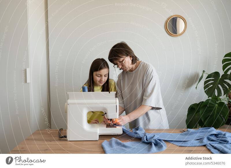 Konzentrierte Frau, die mit einem Mädchen an einer Maschine näht Mutter Tochter lehren nähen Kleid Handwerk Zusammensein Näherin erklären Werkstatt Beruf