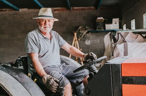 Älterer männlicher Landwirt sitzt auf einem Traktor in einer Garage Mann Porträt Senior Landschaft Ackerbau Maschine gealtert ländlich Fahrzeug schäbig sitzen