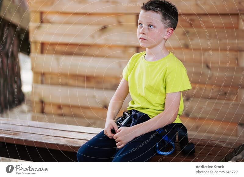 Ruhiger Junge mit Trekkinggürtel in Holzhaus besinnlich Windstille warten Park nachdenklich Seil Konzentration Gurt Bank Kind ernst Sommer lässig sitzen