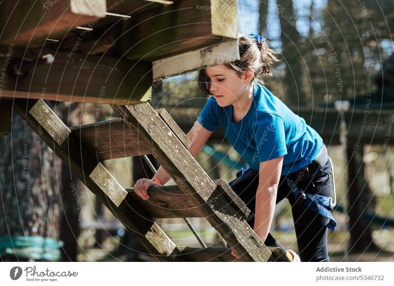 Konzentriertes Mädchen klettert eine Holztreppe im Park hinauf Seil Aufstieg Treppe Podest Aktivität hölzern Kind Sommer Konzentration Sonne lässig aktiv
