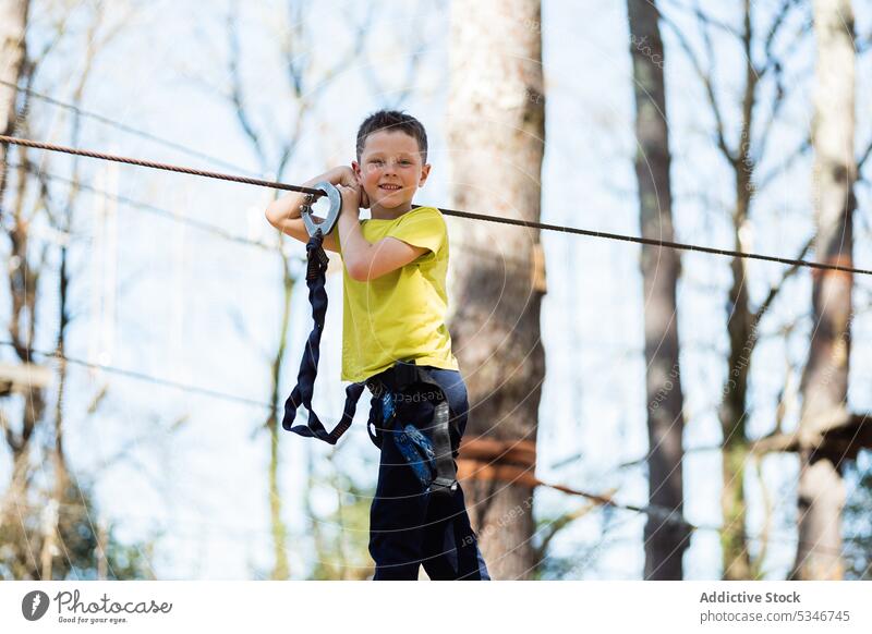 Fröhlicher Junge steht auf einer Seilbrücke im Park Brücke Kind Sommer Sicherheit heiter Natur Gerät Wochenende Aktivität aktiv Kindheit unterhalten Wald