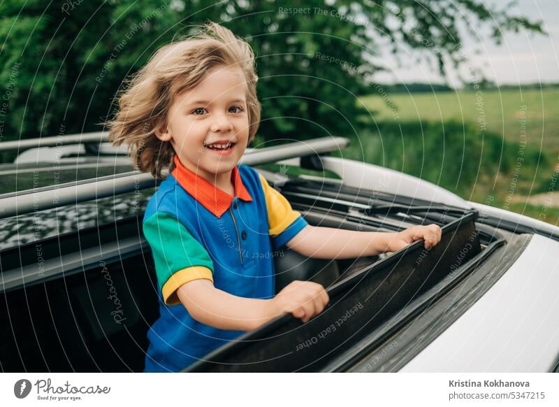 Adorable glücklichen kleinen Jungen steht in offenen Auto Schiebedach während der Reise im Sommer. PKW Kind reisen Familie Menschen Fahrzeug jung sorgenfrei