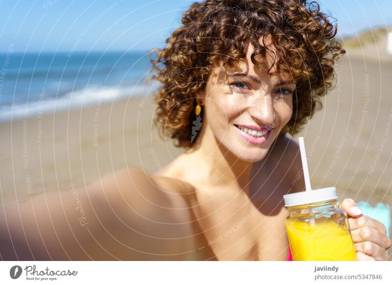 Fröhliche Frau genießt Saft und nimmt Selbstporträt am Strand Selfie trinken Porträt Sommer Urlaub Lächeln Erfrischung sorgenfrei heiter Glück genießen Getränk