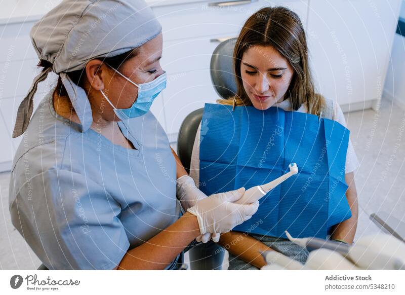 Zahnärztin hält Zahnbürste und spricht mit Patientin Arzt geduldig Frauen Klinik reden Spezialist Zahnarzt Mundschutz Prüfung Krankenpfleger Handschuh