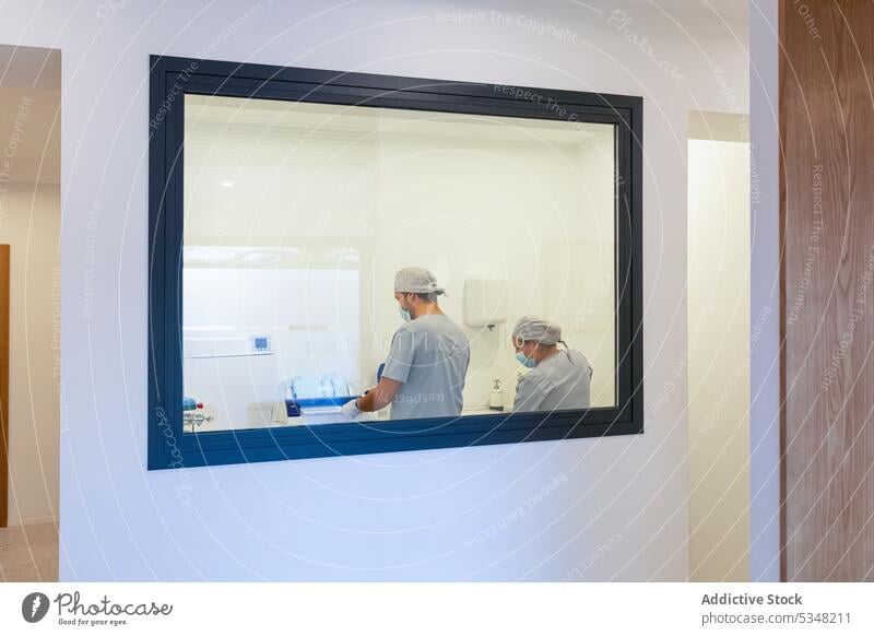 Transparentes Glas zeigt Ärzte mit Maske bei der Arbeit in einem modernen Labor Spezialist Arzt Klinik Kollege Krankenhaus professionell Uniform medizinisch