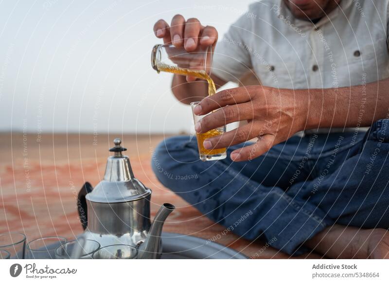 Abgeschnittener Mann serviert heißen Tee in ein Glas Erfrischung eingießen Getränk lokal lässig sitzen Glaswaren Tradition dienen Marrakesch Marokko Heißgetränk