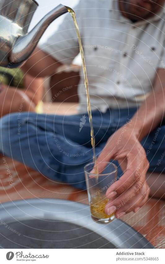 Abgeschnittener Mann gießt heißen Tee in ein Glas Erfrischung eingießen Getränk lokal lässig sitzen Glaswaren Tradition dienen Marrakesch Marokko Heißgetränk