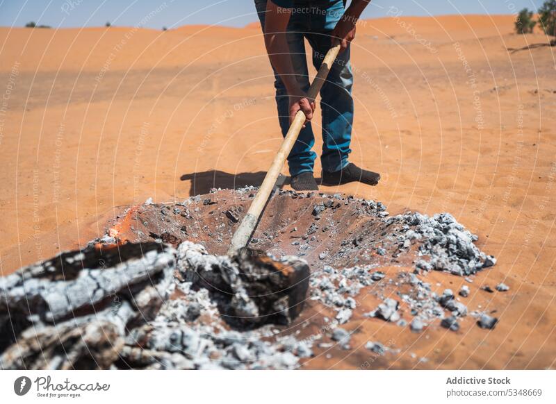 Abgeschnittener Mann bereitet heiße Holzkohle zum Kochen in der Wüste vor Boden Sand vorbereiten Freudenfeuer wüst schaufeln Rauch Marrakesch Marokko Brandwunde