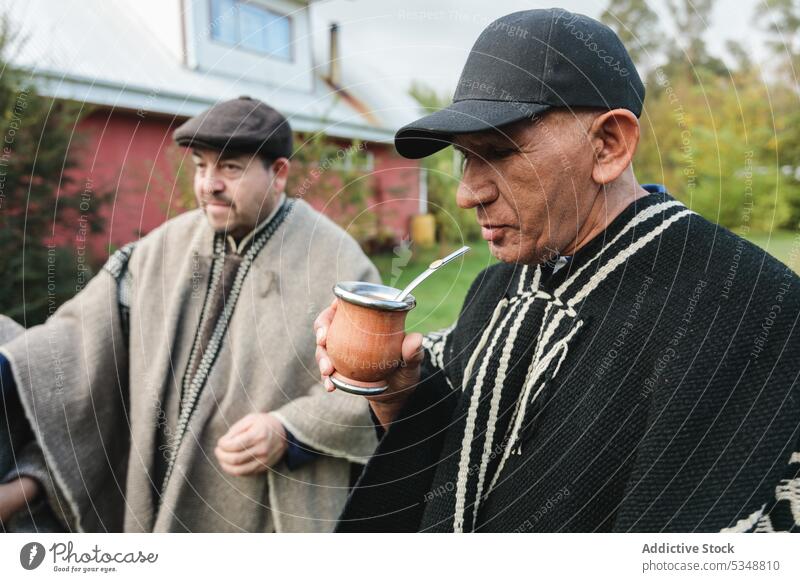 Ältere Freunde in Wollponchos trinken heißen Tee im Park Männer Yerba Partnerin mapuche Zeit verbringen Zusammensein Gras Freundschaft Tradition Rasen Wiese