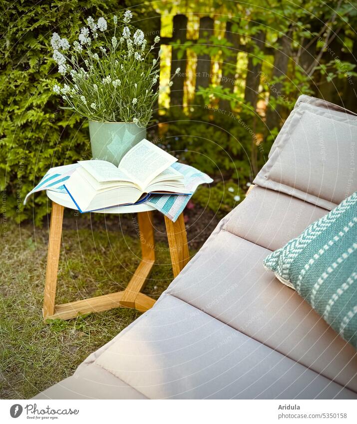 Lieblingsplatz | Liege mit Kissen steht im Garten, daneben steht ein Tisch auf dem ein offenes Buch liegt, dahinter steht ein weißer Lavendel im Topf