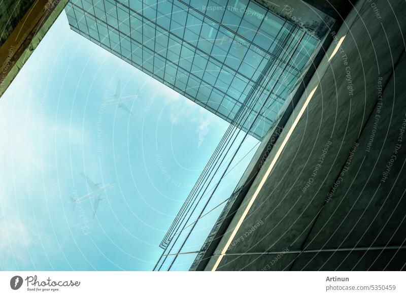 Bottom-up-Ansicht der modernen nachhaltigen Glas-Bürogebäude und Flugzeug fliegen in den blauen Himmel. Außenansicht der Unternehmenszentrale Glasgebäude Architektur. Energieeffizientes Gebäude. Glasfenster