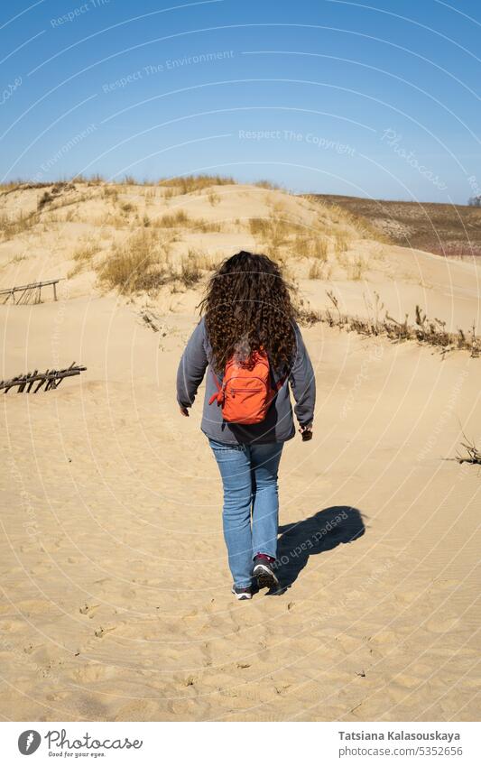 Langhaarige, lockige Frau mit Rucksack auf Sanddünen spazierend Erwachsener Litauen Neringa graue Dünen Tote Dünen sandig Dunes Kurische Nehrung litauisch wüst