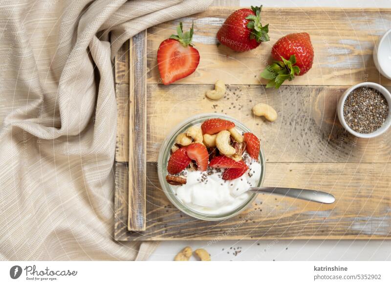 Glasgefäß mit Joghurt, Nüssen und Erdbeeren auf einem Holztablett, Ansicht von oben, Kopierraum Muttern erdbeeren Frühstück hölzern Tablett Draufsicht Löffel