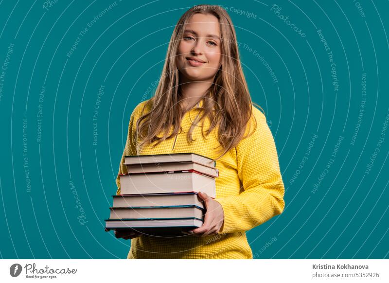 Lächelnde erwachsene Studentin mit Stapel von Büchern aus der Bibliothek auf blauem Hintergrund Amerikaner Waffen attraktiv schön Buch lässig clever Hochschule