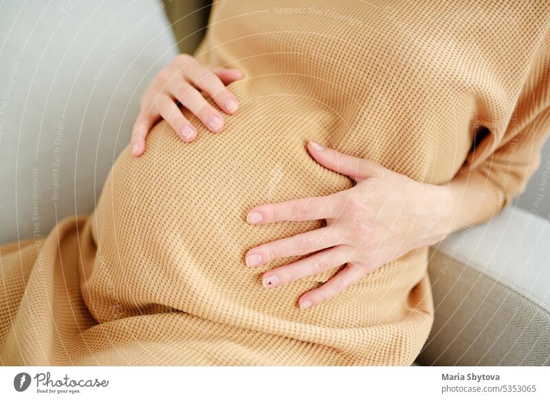 Schwangere kaukasische Frau entspannt sich zu Hause. Junge werdende Mutter streichelt ihren schwangeren Bauch und denkt über das Baby Geburt. erwartungsvoll