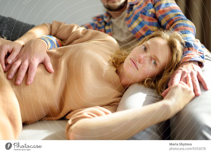 Junge schöne schwangere Frau liegt auf dem Schoß ihres Mannes. Glückliches junges Paar entspannt auf der Couch zu Hause. Angebot Werdende Eltern Werdende Mutter