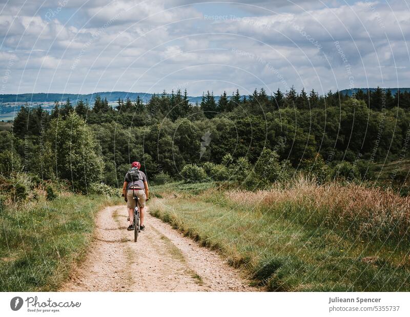 Mann fährt mit dem Fahrrad in Richtung Wald auf einem Feldweg Radfahrer Mann fährt Fahrrad kurz Rucksack Radfahren Radfahren im Gelände Fahrräder Fahrradweg