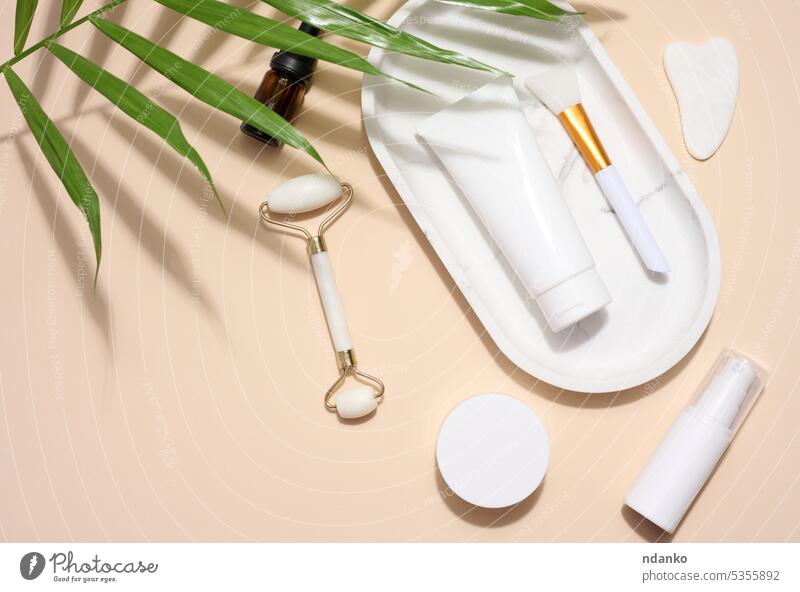 Kunststoffrohr und -gefäß, Jade-Handmassagegerät und Schönheitsbehandlungsschaber auf beigem Hintergrund, Ansicht von oben Glas Nachricht Tube weiß Werbung