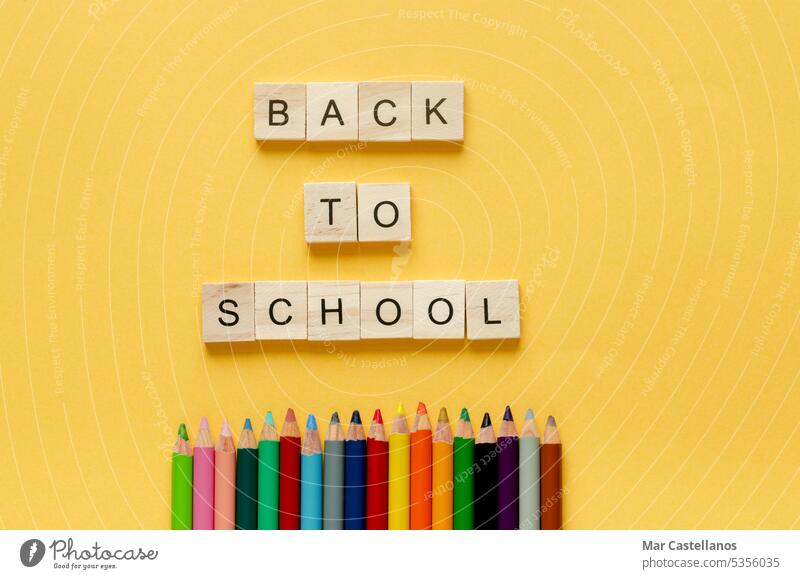 Zurück zum Unterricht. Buntstifte und Buchstaben BACK TO SCHOOL auf gelbem Hintergrund. Platz zum Kopieren. zurück zur Schule Würfel Holz Kuvert