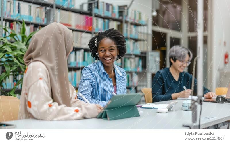Multiethnische Gruppe von Studenten, die in einer Bibliothek sitzen und gemeinsam lernen echte Menschen Teenager Campus positiv Prüfung Wissen selbstbewusst