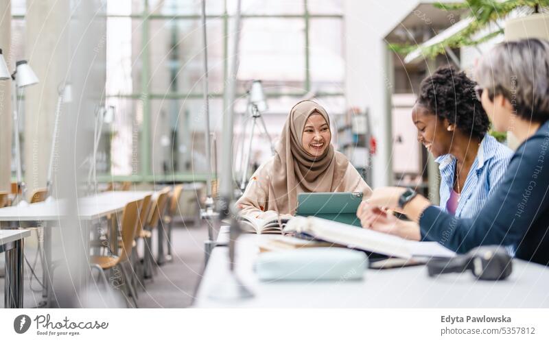 Multiethnische Gruppe von Studenten, die in einer Bibliothek sitzen und gemeinsam lernen echte Menschen Teenager Campus positiv Prüfung Wissen selbstbewusst