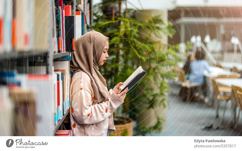 Junge asiatische muslimische Frau liest ein Buch in einer Bibliothek echte Menschen Teenager Campus positiv Prüfung Wissen selbstbewusst schulisch Erwachsener