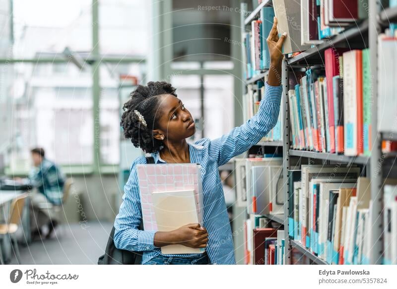Schwarze Studentin nimmt ein Buch aus dem Bücherregal in der Bibliothek echte Menschen Teenager Campus positiv Prüfung Wissen selbstbewusst schulisch