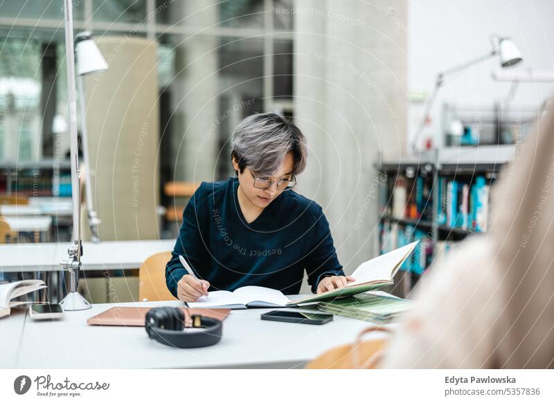 Asiatische Studentin schreibt am Tisch in der Bibliothek in ein Notizbuch echte Menschen Teenager Campus positiv Prüfung Wissen selbstbewusst schulisch