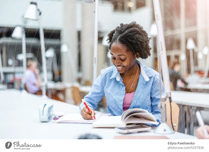 Junge schwarze Frau schreibt in einer Bibliothek in ein Notizbuch echte Menschen Teenager Campus positiv Prüfung Wissen selbstbewusst schulisch Erwachsener