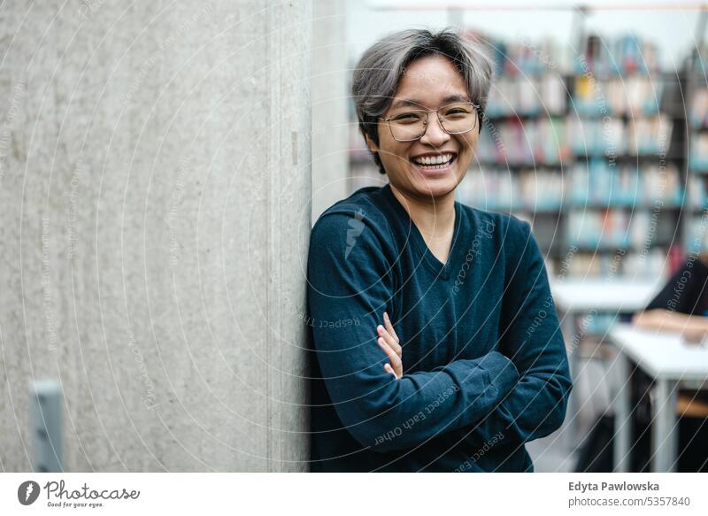 Porträt eines lächelnden asiatischen Studenten, der mit verschränkten Armen in einer College-Bibliothek steht echte Menschen Teenager Campus positiv Prüfung
