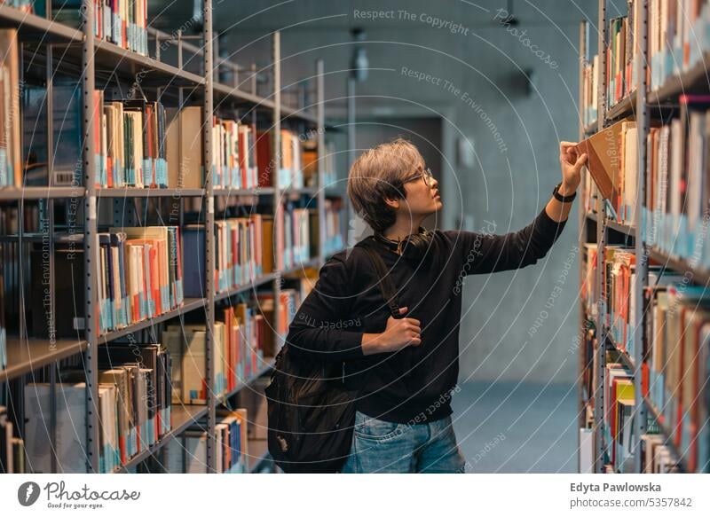 Porträt eines asiatischen Studenten, der ein Buch aus dem Bücherregal in der Bibliothek nimmt echte Menschen Teenager Campus positiv Prüfung Wissen
