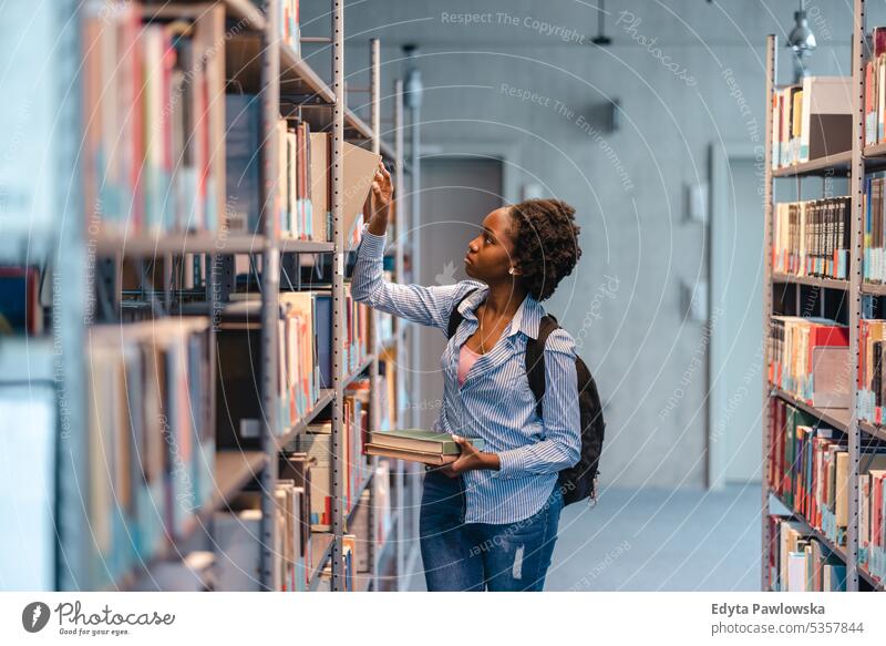 Schwarze Studentin nimmt ein Buch aus dem Bücherregal in der Bibliothek echte Menschen Teenager Campus positiv Prüfung Wissen selbstbewusst schulisch