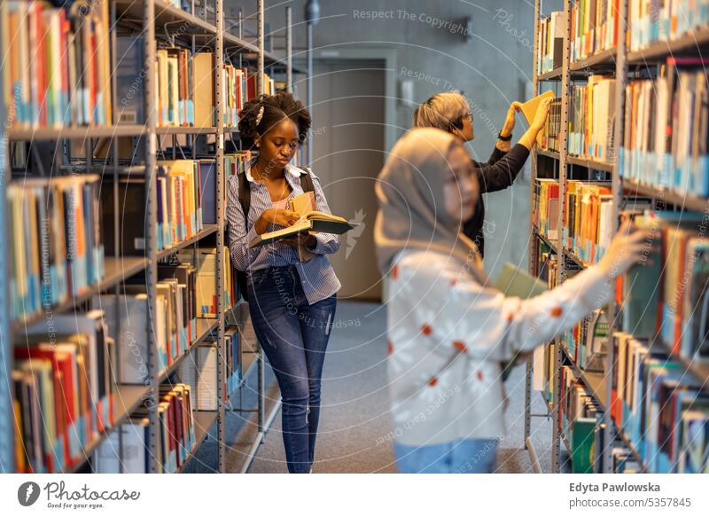 Gruppe multiethnischer Studenten, die in einer Bibliothek Bücher aus dem Regal nehmen echte Menschen Teenager Campus positiv Prüfung Wissen selbstbewusst
