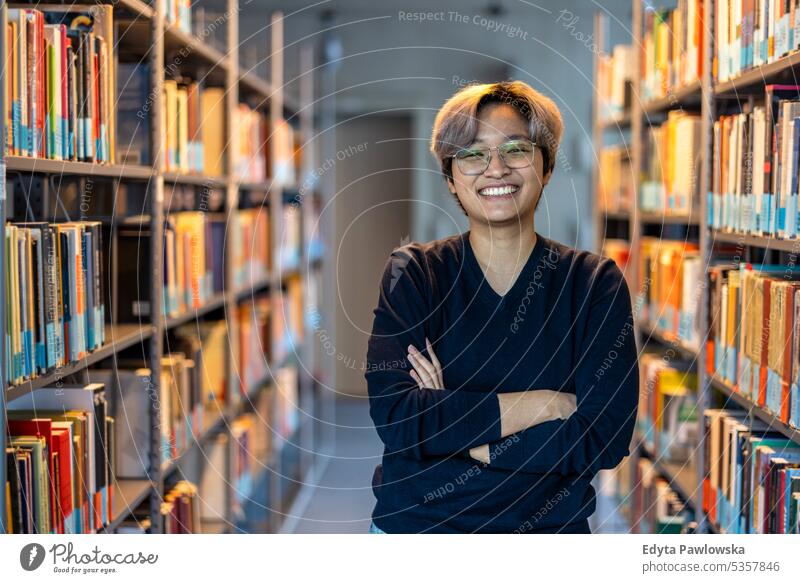 Porträt eines lächelnden asiatischen Studenten, der mit verschränkten Armen in einer College-Bibliothek steht echte Menschen Teenager Campus positiv Prüfung