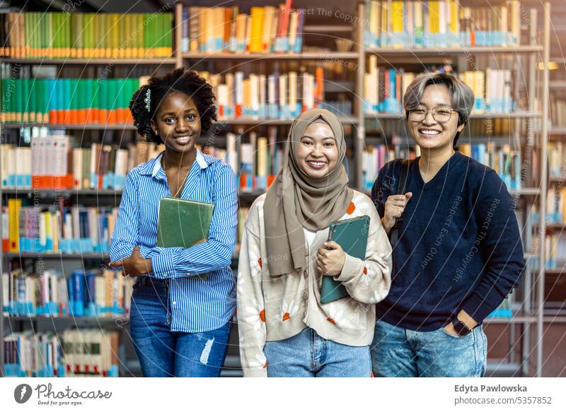 Eine Gruppe verschiedener Studenten lächelt in die Kamera, während sie zusammen in einer Bibliothek stehen echte Menschen Teenager Campus positiv Prüfung Wissen